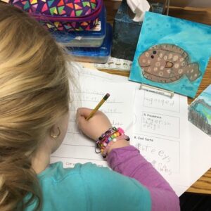A student writes her story after creating images in the research-based animal trifold unit.